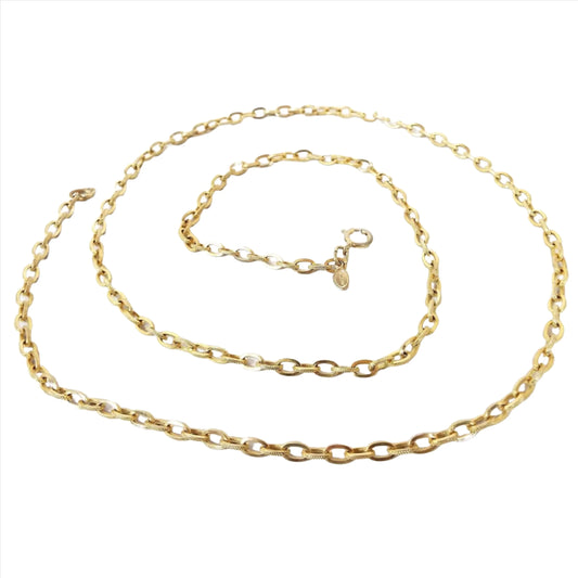 Top view of the retro 1970's Avon vintage chain necklace. Metal is gold tone in color. Necklace has oval cable link design with textured edges on the links. There is around spring ring clasp on the end and an oval hang tag that has Avon marked on it.