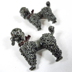 Front view of the 1950's Mid Century vintage poodle brooch pin set. Both brooches have a side view of a gray enameled poodle dog with reddish brown eyes and ribbon tied around their necks. One brooch is larger than the other. 