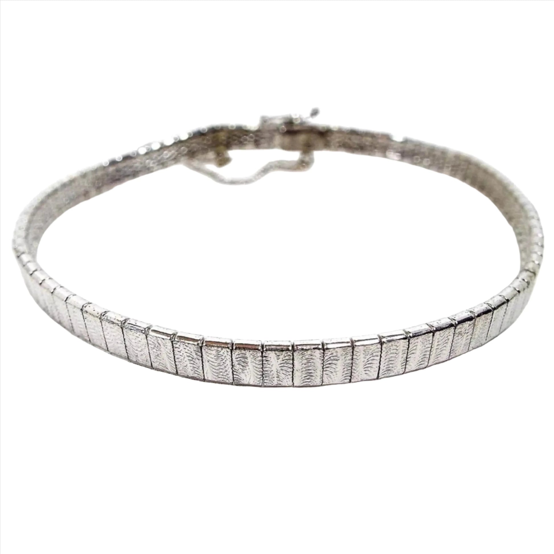 Bracelet with small silver color rectangle interlocked links. Each link has a stamped fern leaf style pattern. It has a locking clasp with a small chain on the side.