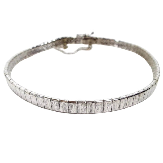 Bracelet with small silver color rectangle interlocked links. Each link has a stamped fern leaf style pattern. It has a locking clasp with a small chain on the side.