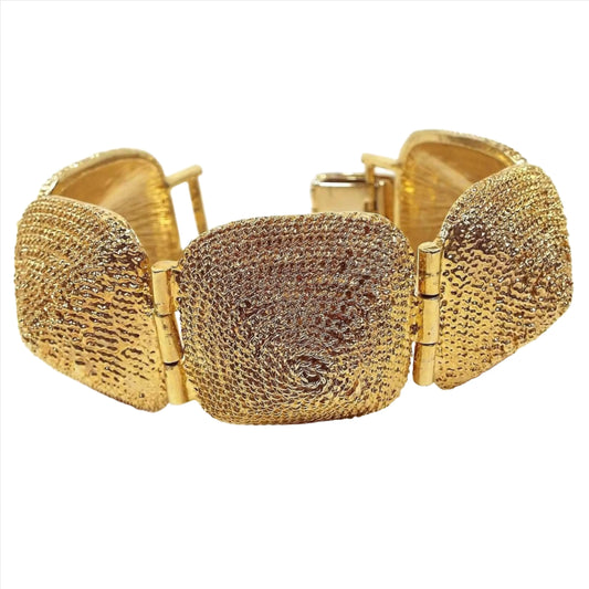 Front view of the retro vintage wide link bracelet. There are five large links that are rounded square in shape and domed. Each one has a textured spiral design on it. It is gold tone in color and there is a snap lock clasp on the end.