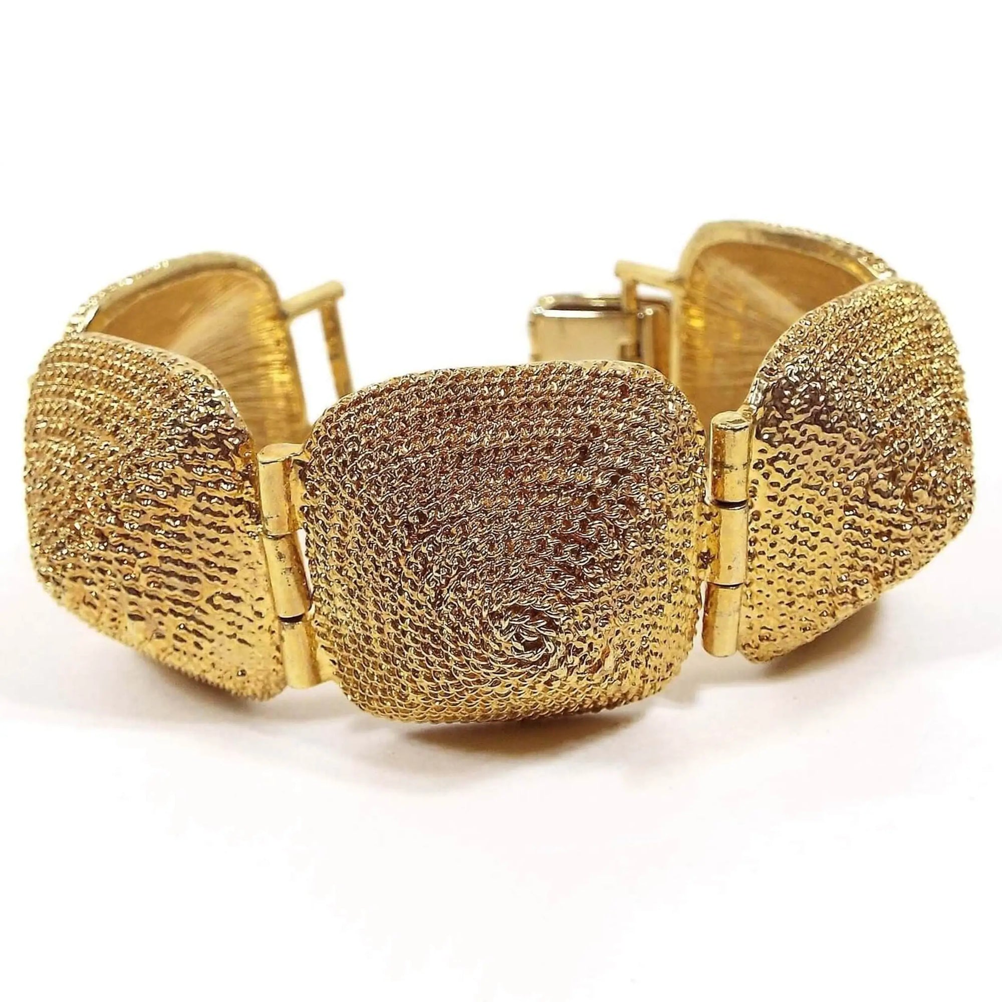 Front view of the retro vintage wide link bracelet. There are five large links that are rounded square in shape and domed. Each one has a textured spiral design on it. It is gold tone in color and there is a snap lock clasp on the end.