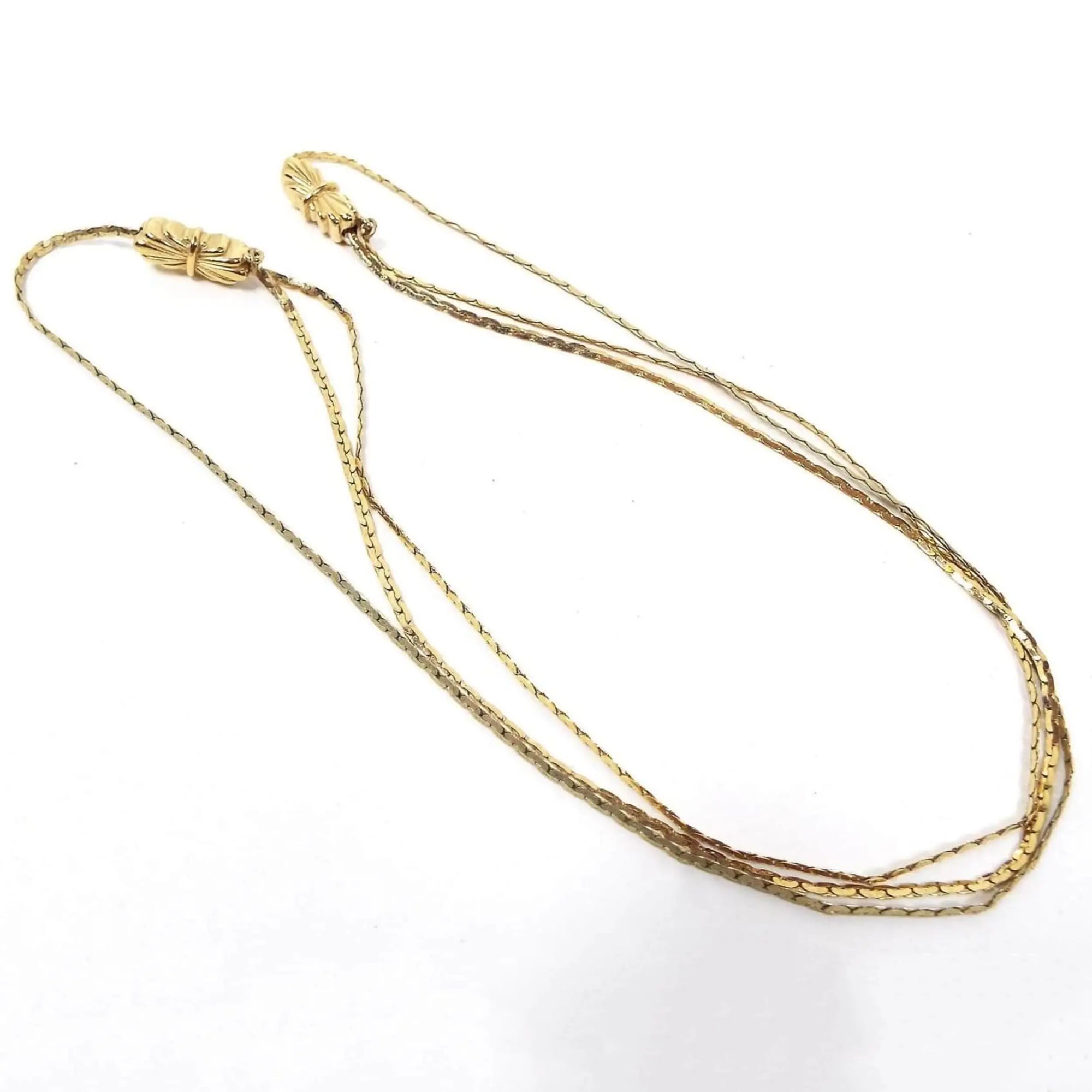 Top view of the retro vintage chain necklace. The C link chain is gold tone in color. There are two bow like slide links towards the top of the necklace that slide up and down the chain to adjust the length. The bottom part of the necklace has two strands that also can be made longer or shorter when adjusting the chain.