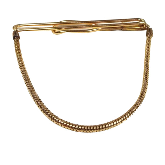 Front view of the 1940's Mid Century vintage Swank tie chain bar. It is gold tone in color. The top has a long open oval wire bar that curves around to the back with a larger open oval area on the end. Snake chain comes down from either side to hang in a curve at the bottom.