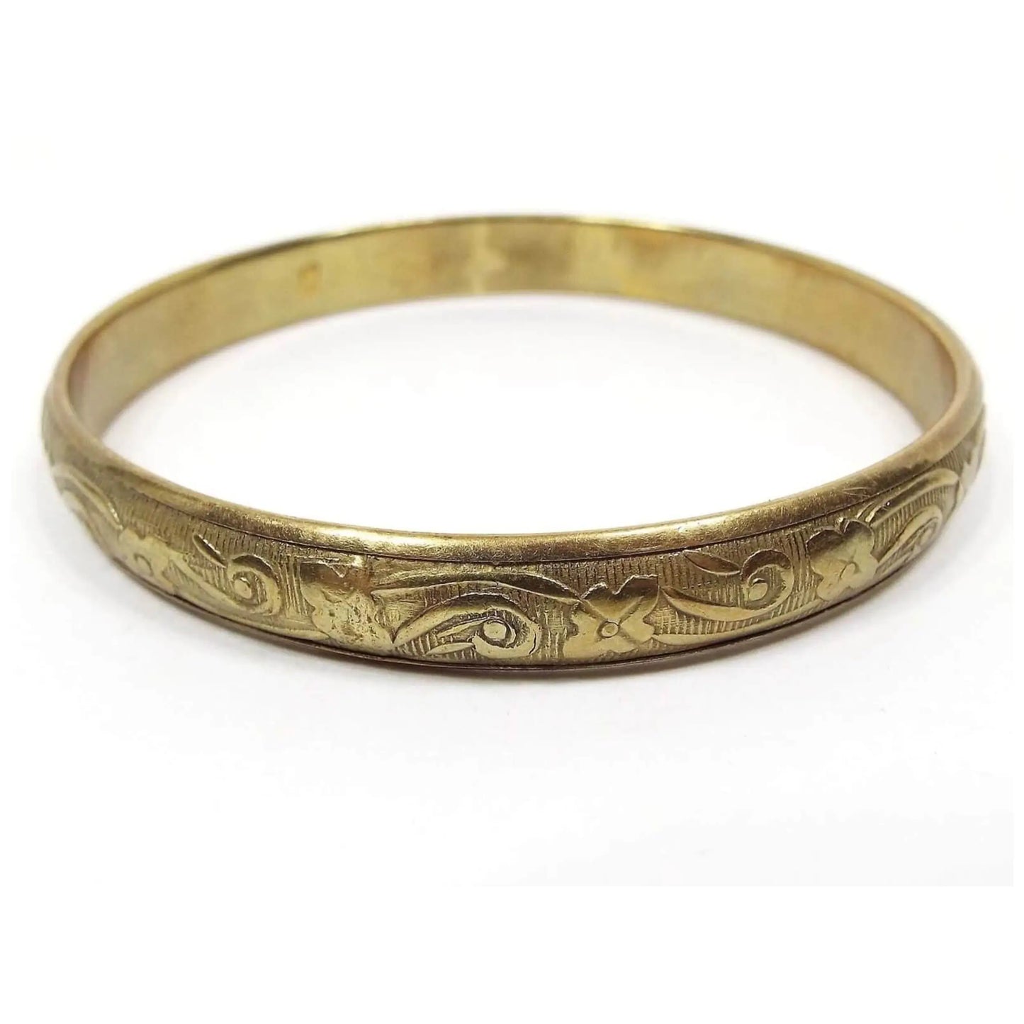 Angled side and top view of the retro vintage floral bangle bracelet. It's made of brass and is a darker gold tone in color. The bangle is round with a raised pattern of flowers against a background of lines.