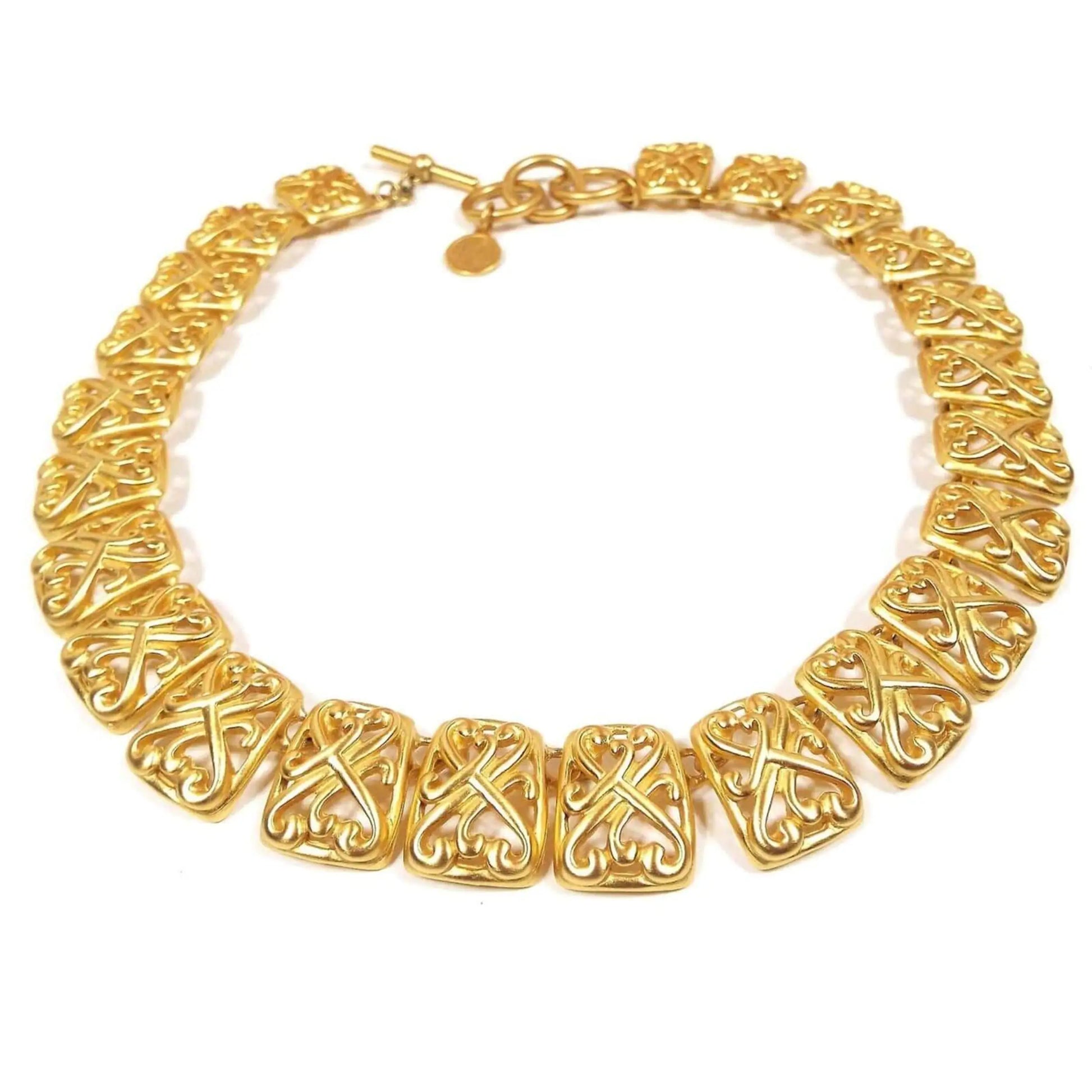 Top view of the retro vintage Anne Klein link necklace. It is gold tone in color with large rectangle links that have a curvy filigree design. There is a toggle clasp at the end with three large rings for it to go through to adjust the length.