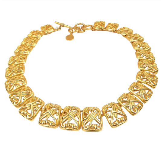 Top view of the retro vintage Anne Klein link necklace. It is gold tone in color with large rectangle links that have a curvy filigree design. There is a toggle clasp at the end with three large rings for it to go through to adjust the length.