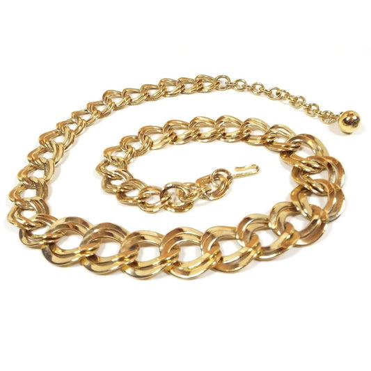 Top view of the retro vintage chain link necklace. The metal is gold tone in color. It has wide double curb links that are curvy oval shaped. The links are graduated in size from largest in the middle down to the smallest at the ends. There is a hook clasp on one end and a gold tone round bead at the other.