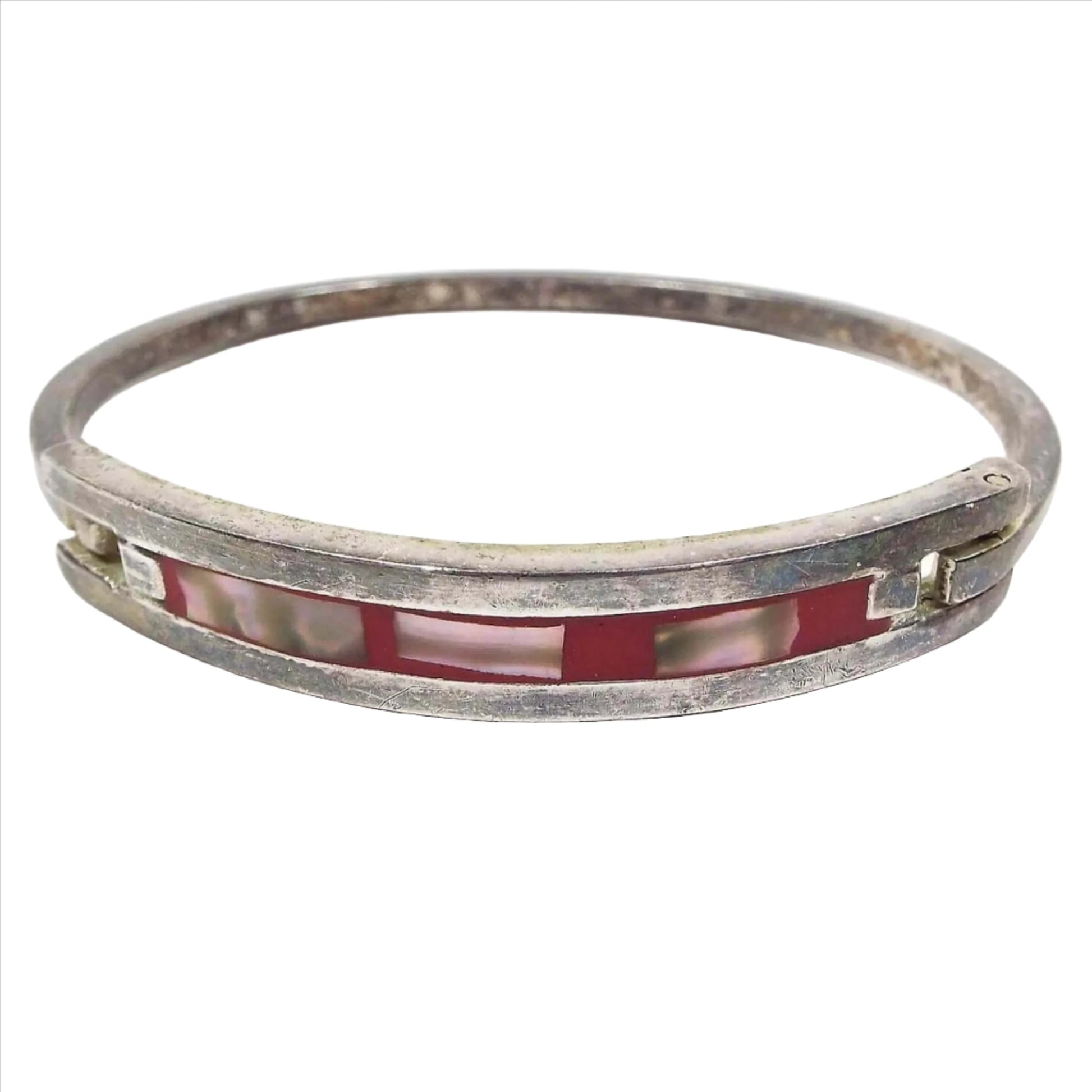 Front view of the retro vintage Mexican hinged bangle bracelet. The front has a channel with red enamel and free form style rectangle shaped pieces of inlaid abalone shell. the metal is darkened silver in color from age.