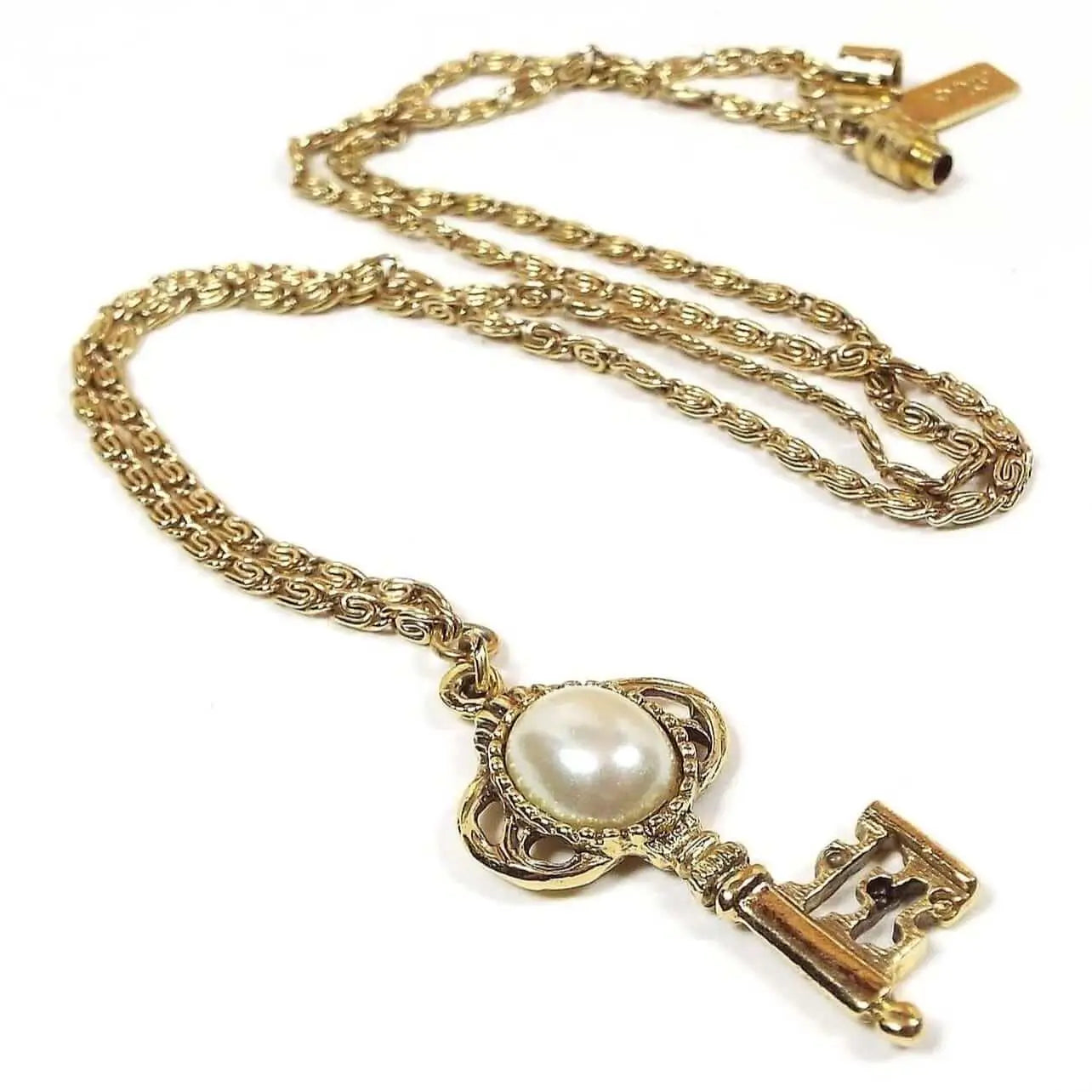 Chain is gold in color with snail links that look like the letter S. It has an oval barrel screw on clasp. The pendant is gold color old style skeleton key with rounded oval pearly off white plastic at the top. There is a rectangle tag that is stamped 1928 on it.