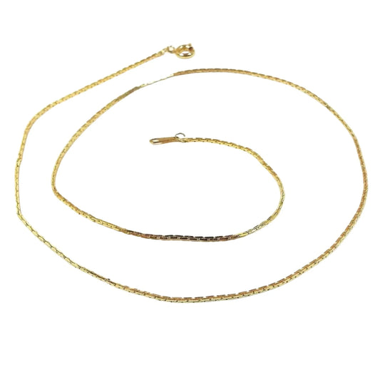 Chain is gold in color with small square links. Each link alternates between the square being up and down or sideways. Clasp is a round spring ring clasp.