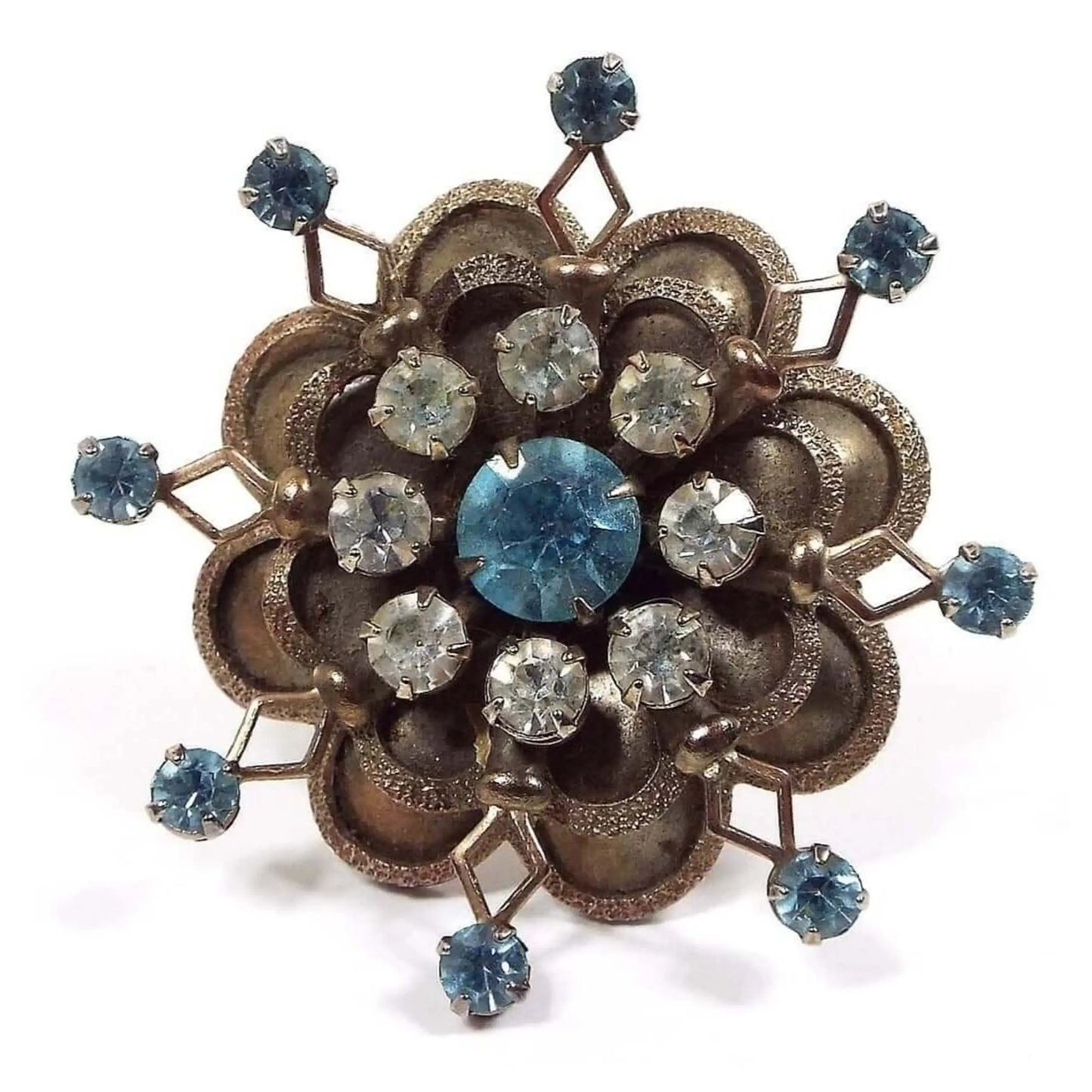 Front view of the 1950's Mid Century vintage rhinestone brooch pin. Brooch has a flower like starburst design. Middle rhinestone is round with light blue color and is surrounded by smaller round clear rhinestones. Some of the clear rhinestones are lightly cloudy and not perfectly clear. There are two layers of small rounded petals around the edge with textured edges. The bottom layer of petals has an open diamond shape in between each petal with a small round light blue rhinestone at the end of each.