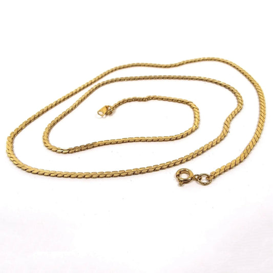 Top view of the retro vintage chain necklace. The metal is gold tone in color. It has serpentine style flat links with a round spring ring clasp showing on the end.