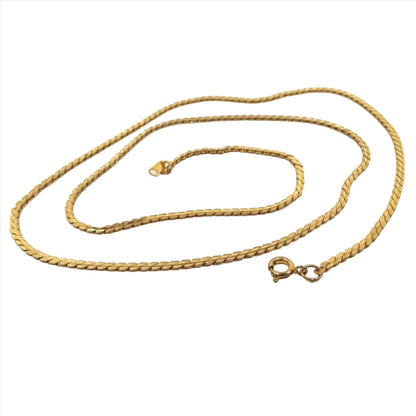 Top view of the retro vintage chain necklace. The metal is gold tone in color. It has serpentine style flat links with a round spring ring clasp showing on the end.