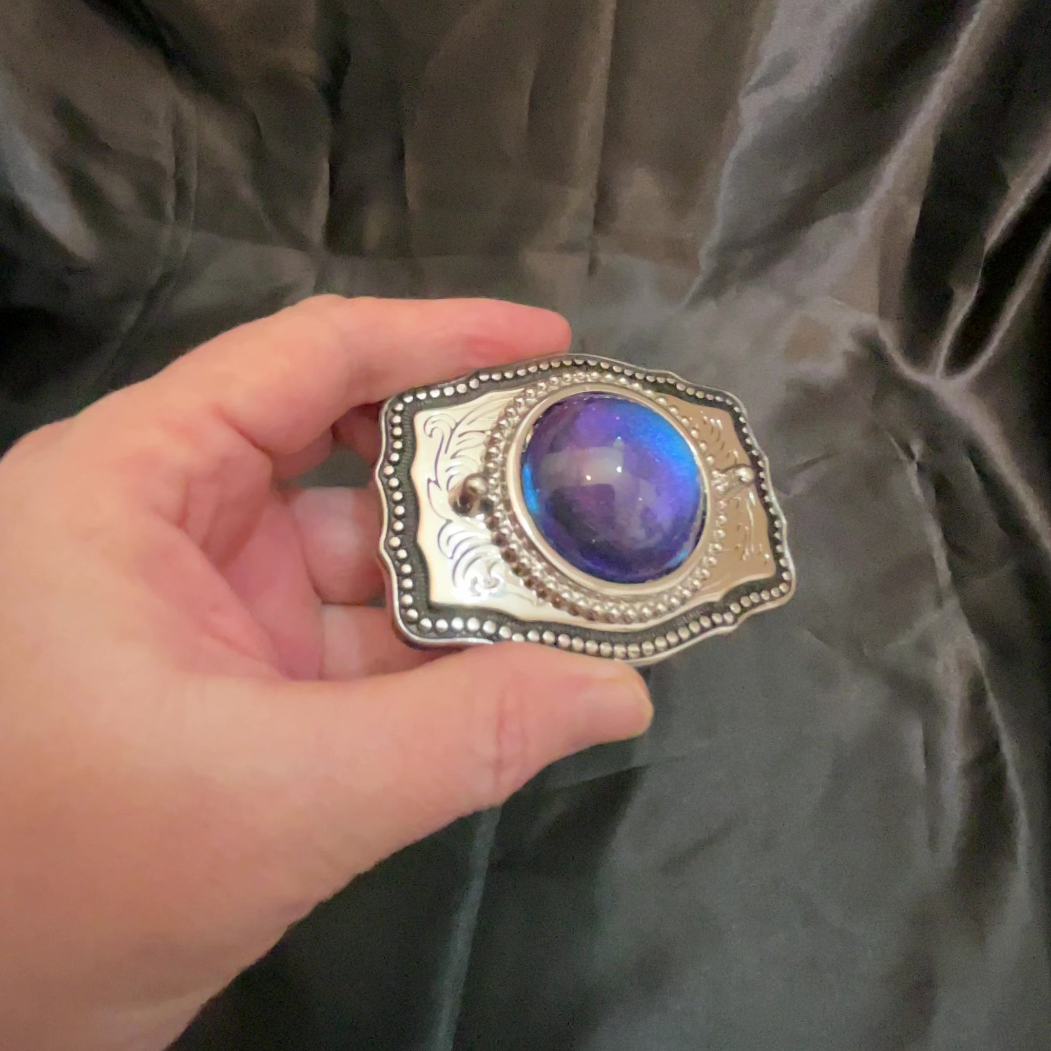 Video of the upcycled belt buckle with domed round cab showing how the color shift design goes from blue to purple depending on how the light hits it.