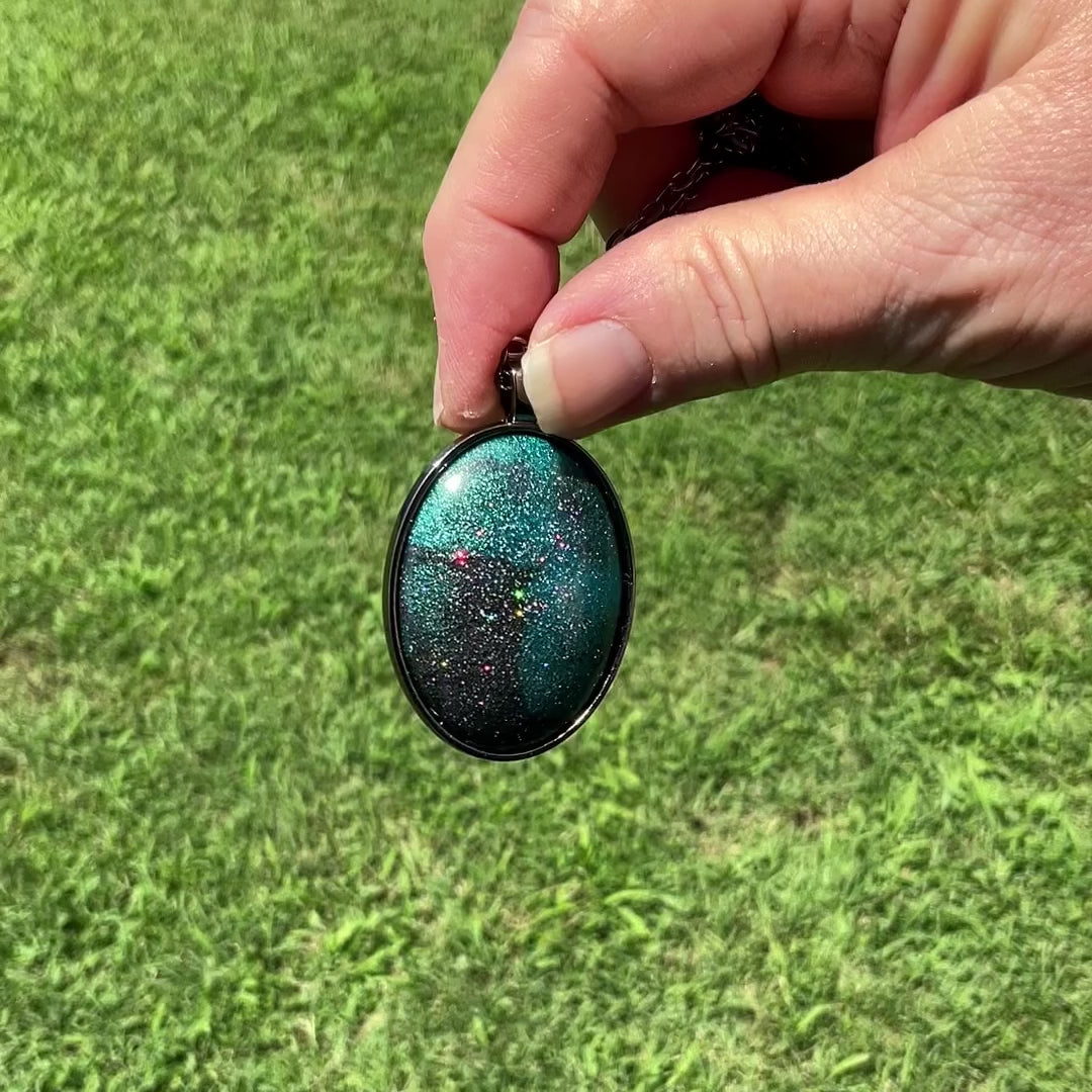 Handmade Dark Gray and Teal Blue Resin Oval Pendant Necklace with Holo Glitter video showing how the glitter flashes sparkles of color as it moves around in the light.