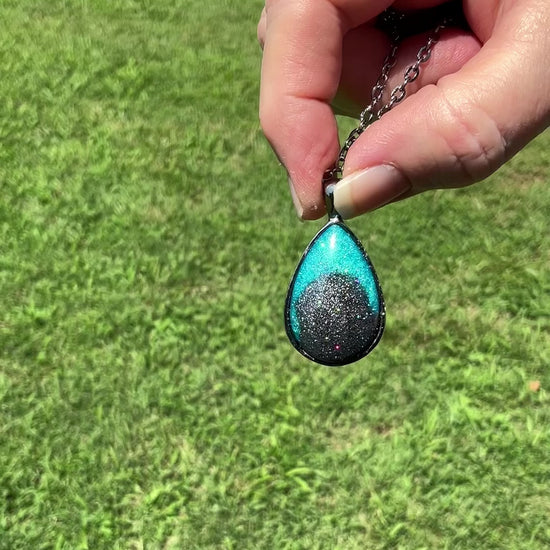 Handmade Teal Blue and Dark Gray Resin Teardrop Pendant Necklace with Holographic Glitter video showing how the glitter sparkles and has flashes of color in the light.