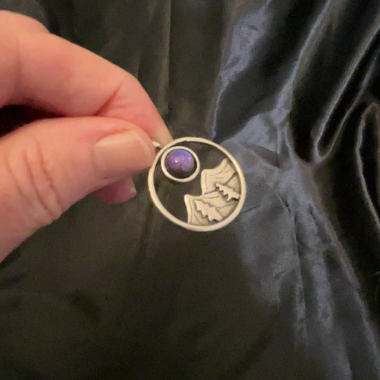 Video of the mountain and trees pendant necklace showing how the handmade resin cab color shifts from blue to purple depending on how the light hits it.