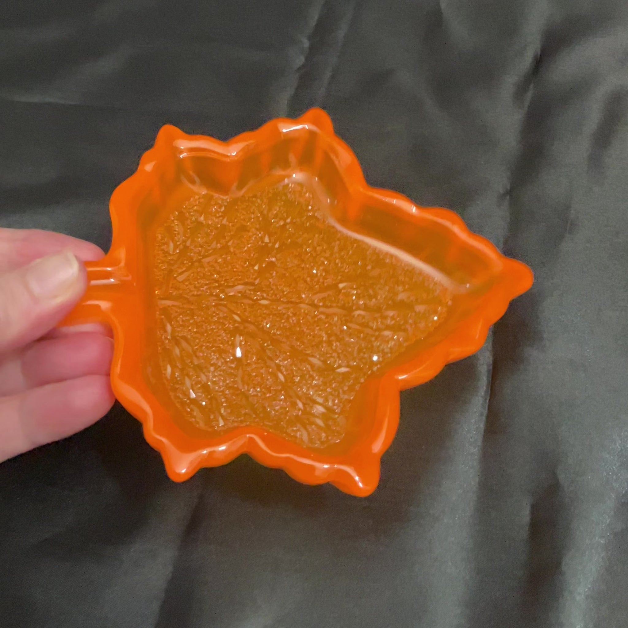 Video showing how the neon orange handmade resin leaf decorative tray has a sparkly crystal like bottom as the light hits it.