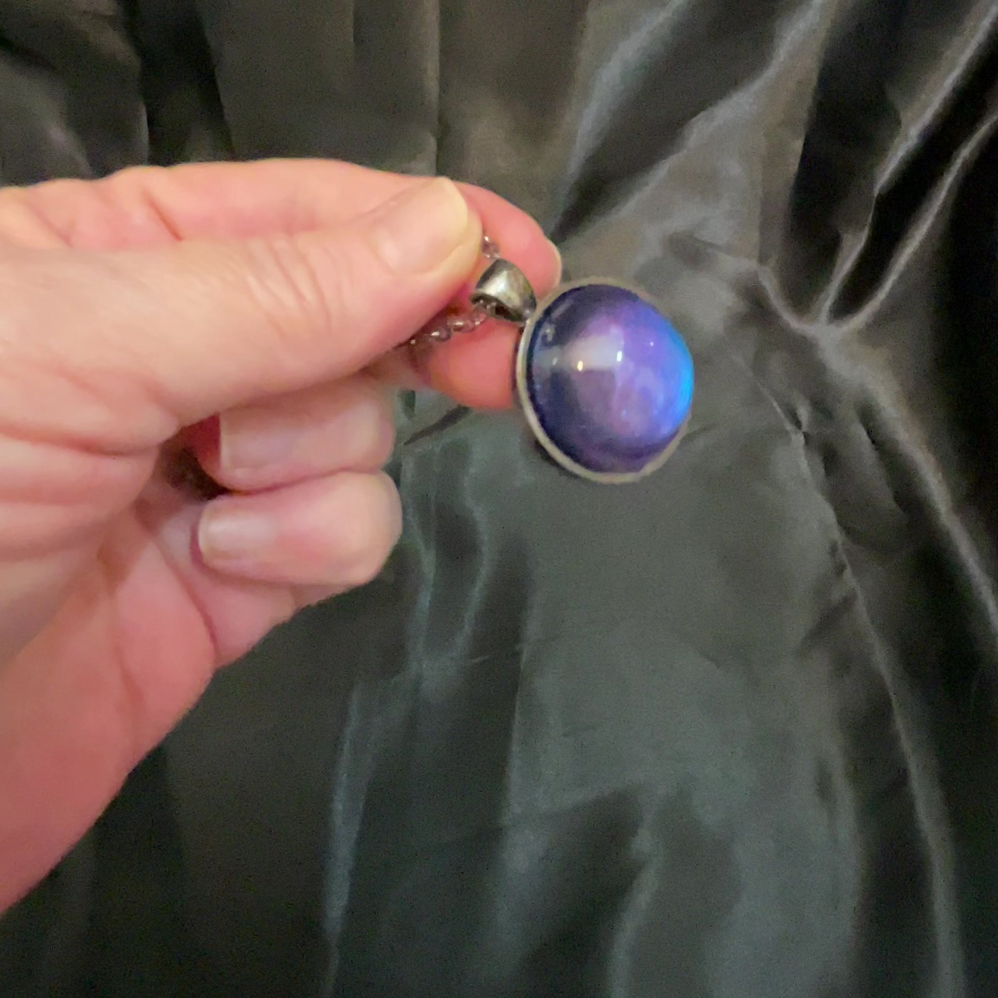 Video showing how the gunmetal plated handmade round resin color shift pendant shifts from blue to purple depending on how the light hits it.