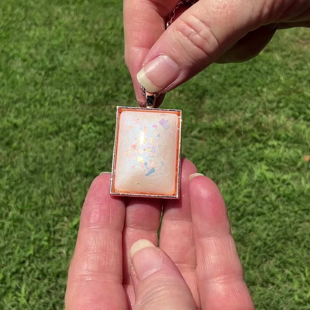Handmade Blue Opal Color Shift Resin with AB Pink Glitter Rectangle Pendant Necklace video showing one of the rose gold plated styles. The video shows how the glitter sparkles in the light as it moves around.
