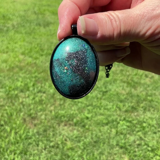 Handmade Dark Gray and Teal Blue Resin Black Oval Pendant Necklace with Holo Glitter video showing how the glitter flashes and sparkles in the light.