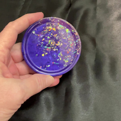 Video of the handmade round purple and pink resin trinket dish with iridescent flakes showing how it sparkles and has flashes of color in the light.