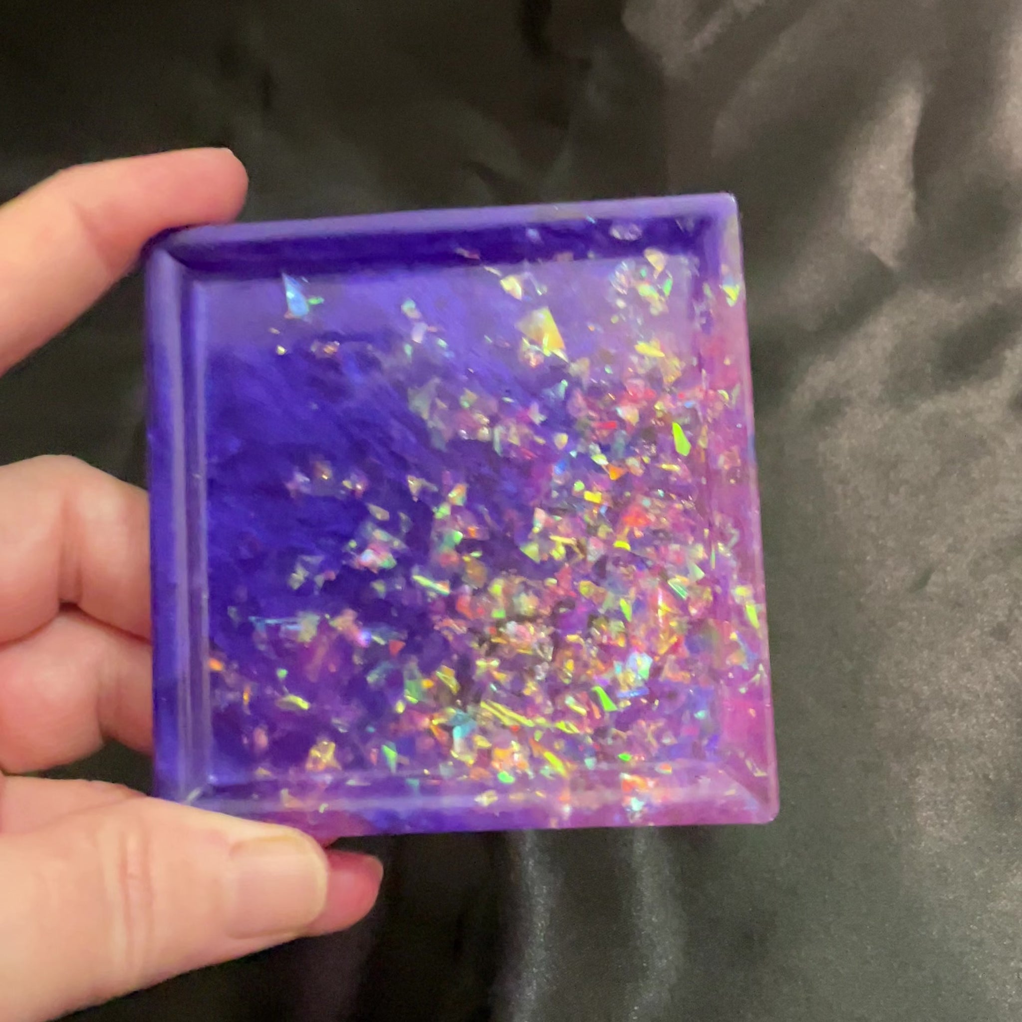 Video of the handmade square purple and pink resin trinket dish with iridescent flakes showing how it sparkles and has flashes of color in the light.