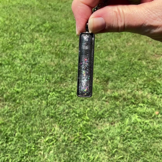 Gunmetal Gray Handmade Resin Bar Pendant Necklace with Holographic Glitter video showing how the glitter has flashes and sparkle of color as it moves around in the light.