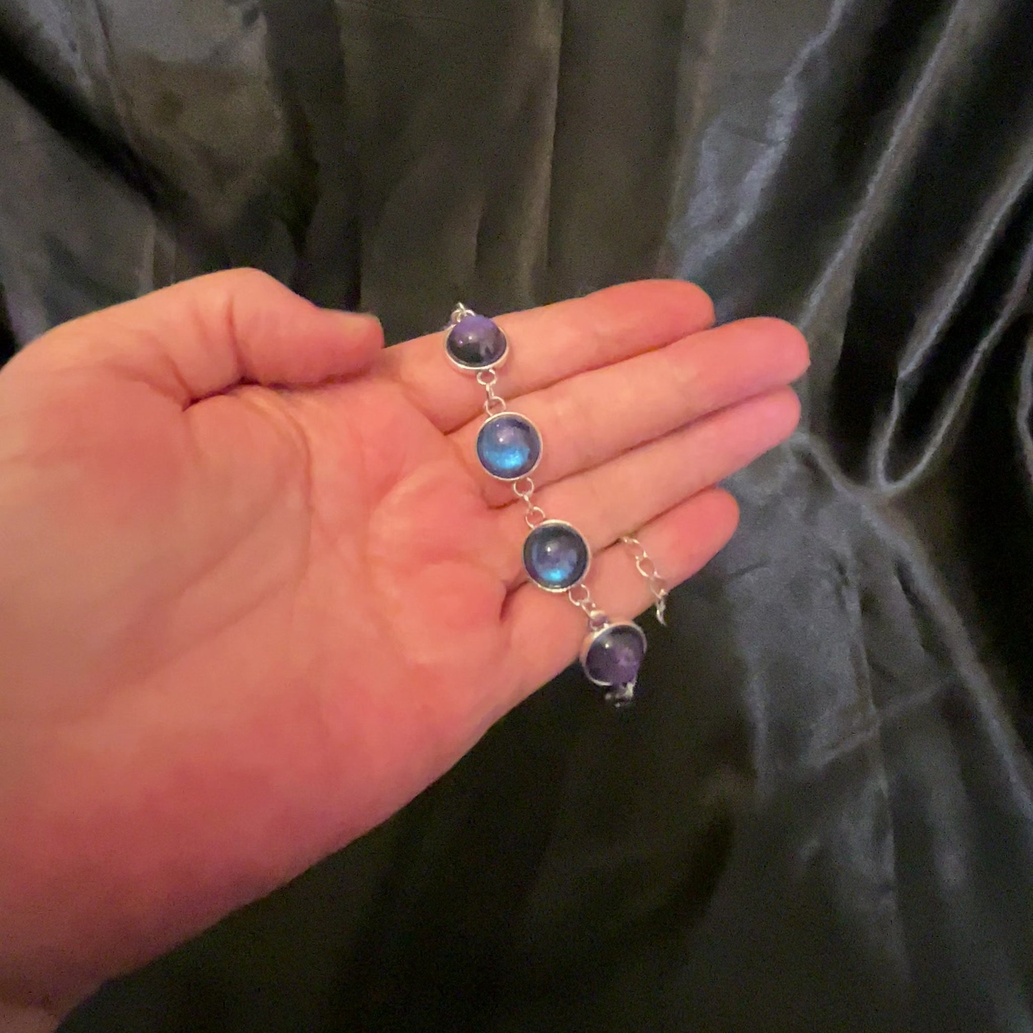 Video showing how the handmade link bracelet domed round resin cabs color shift from blue to purple as the light hits it.