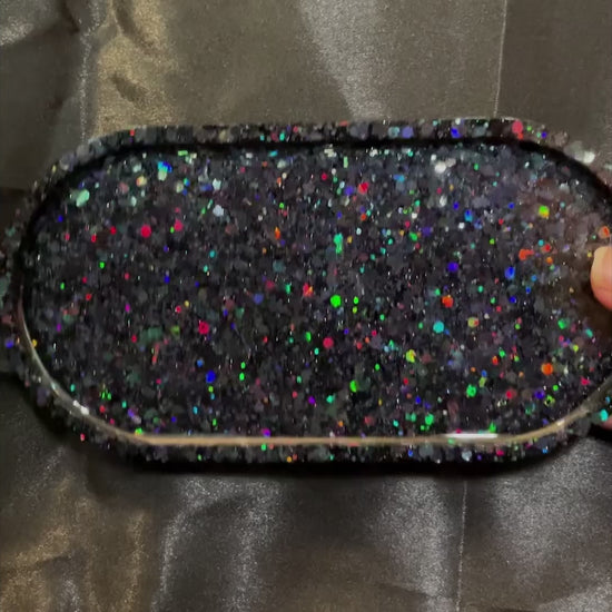 video of the handmade black resin Goth oval trinket dish showing how the rainbow iridescent glitter sparkles in the light.