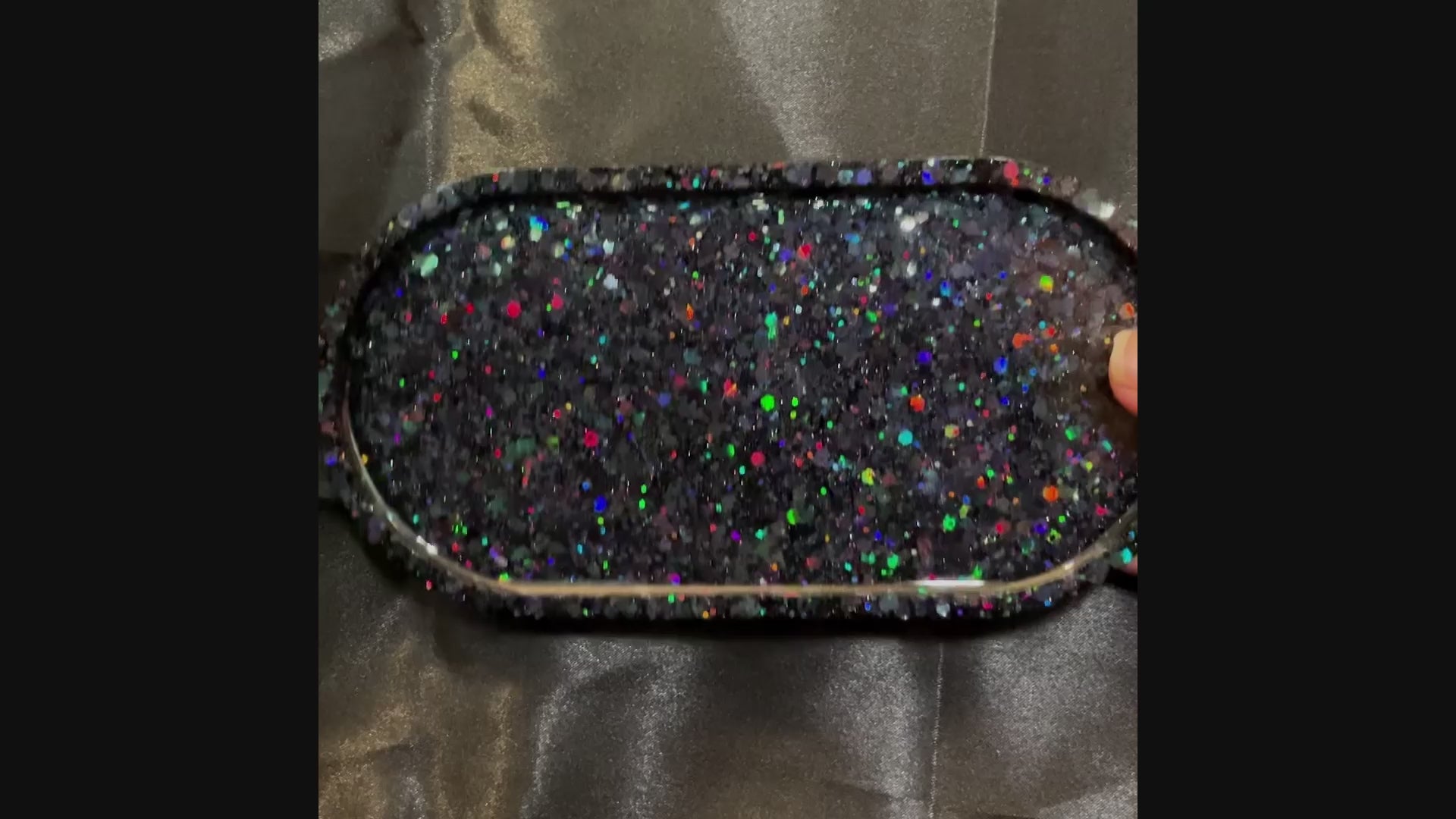 video of the handmade black resin Goth oval trinket dish showing how the rainbow iridescent glitter sparkles in the light.