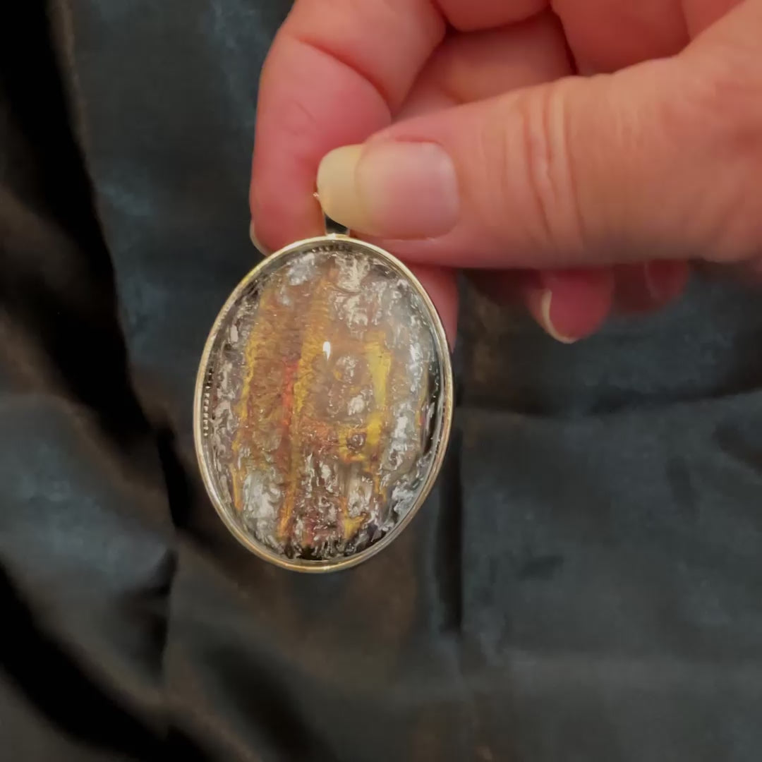 Video of the handmade pendant made with vintage abalone and resin cabs. The metal is silver in color and there is a large oval pendant hanging from the chain. The cab has iridescent colors of green, red, and brown and there are areas of frosty white on the top layers of resin.