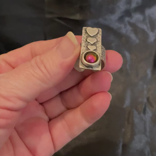 Video of the color shift adjustable heart ring showing how the resin cab shifts from pink to green, orange, and yellow depending on how the light is hitting it.