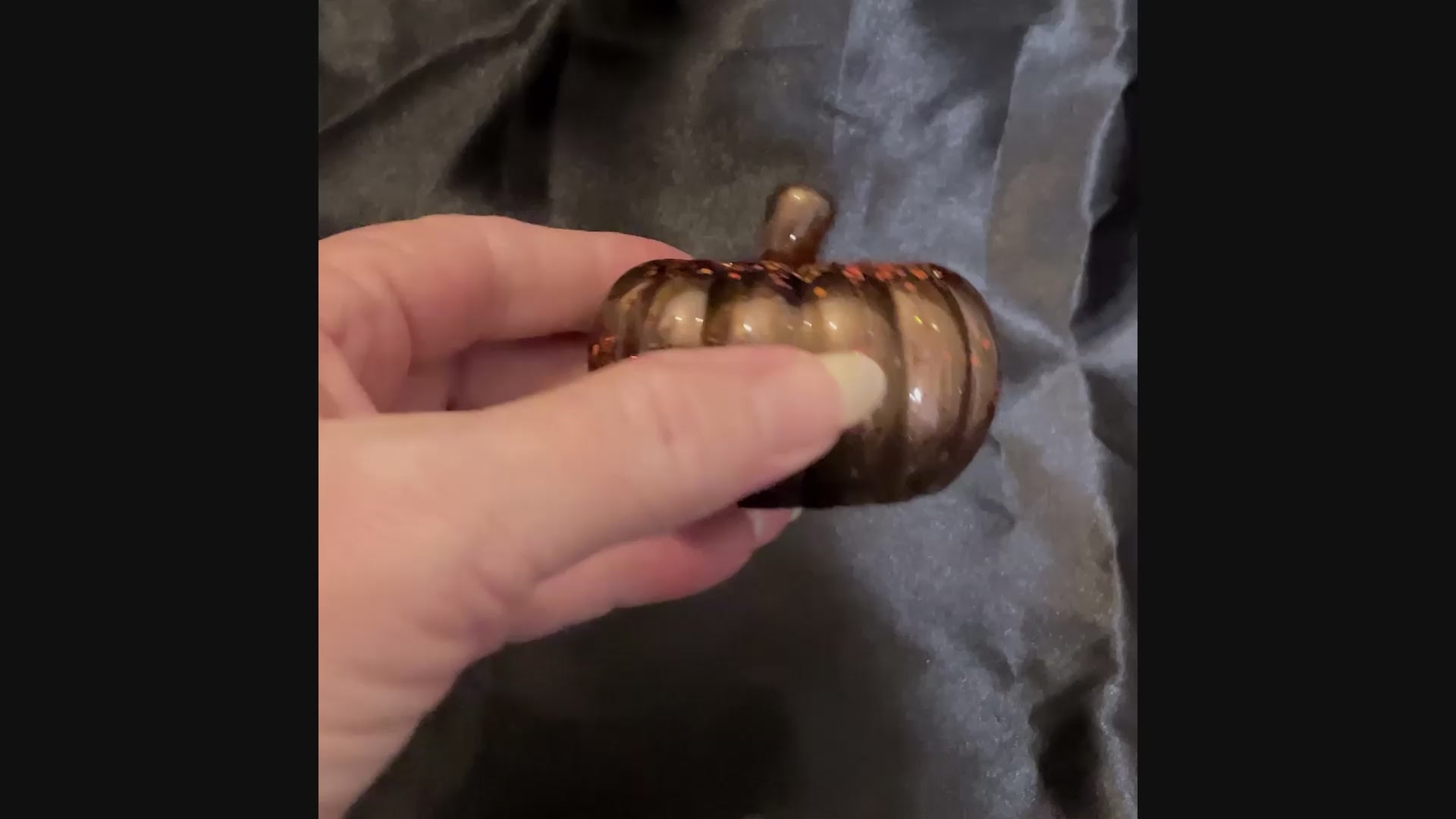 Video showing how the iridescent orange chunky glitter sparkles on the small handmade dark brown resin pumpkin.