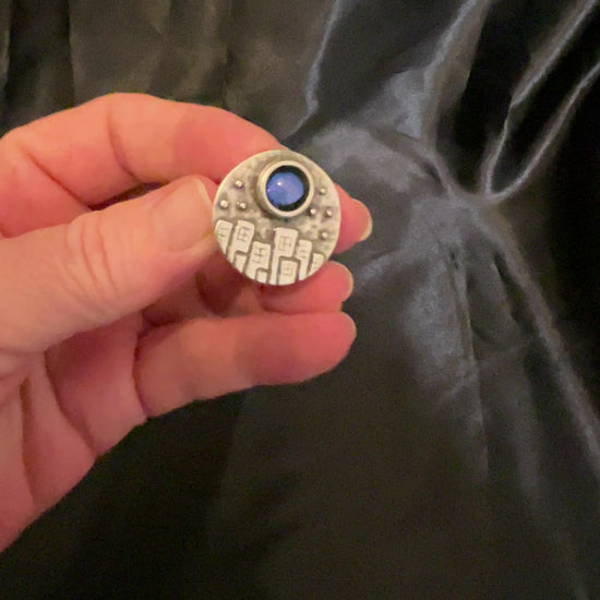 Video of the handmade city at night adjustable ring showing how the color shift resin cab goes from blue to purple as the light hits it.