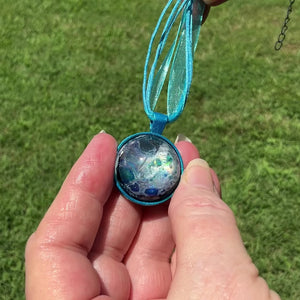 Handmade Round Aqua Blue Resin Pendant Necklace with Abstract Design video showing how the design has flashes of color shift as it moves around in the light.