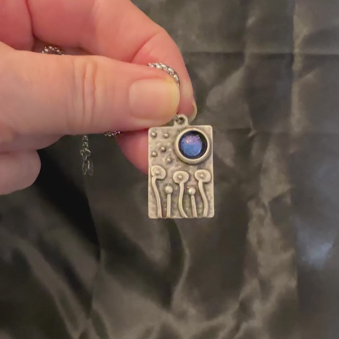 Video of the color shift primitive flower pendant showing how the color goes from blue to purple depending on how the light hits it.