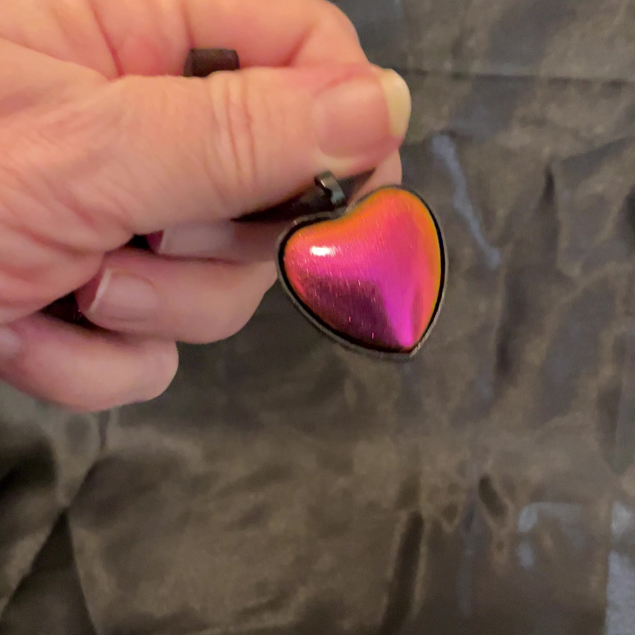 Video of the pink, orange, and yellow matte metallic color shift black heart necklace showing how the colors shift as it moves around in the light.