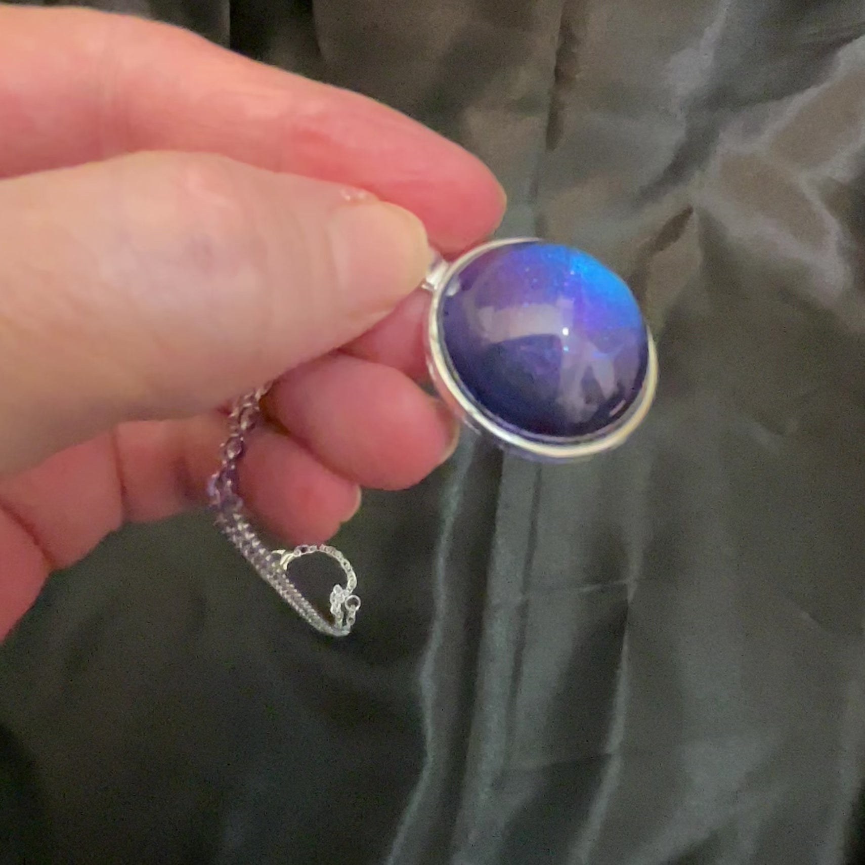 Video showing how the silver plated handmade round resin color shift pendant shifts from blue to purple depending on how the light hits it.