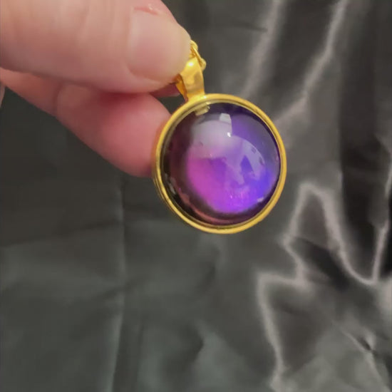 Video showing how the gold plated handmade round resin color shift pendant shifts from blue to purple and other colors depending on how the light hits it.