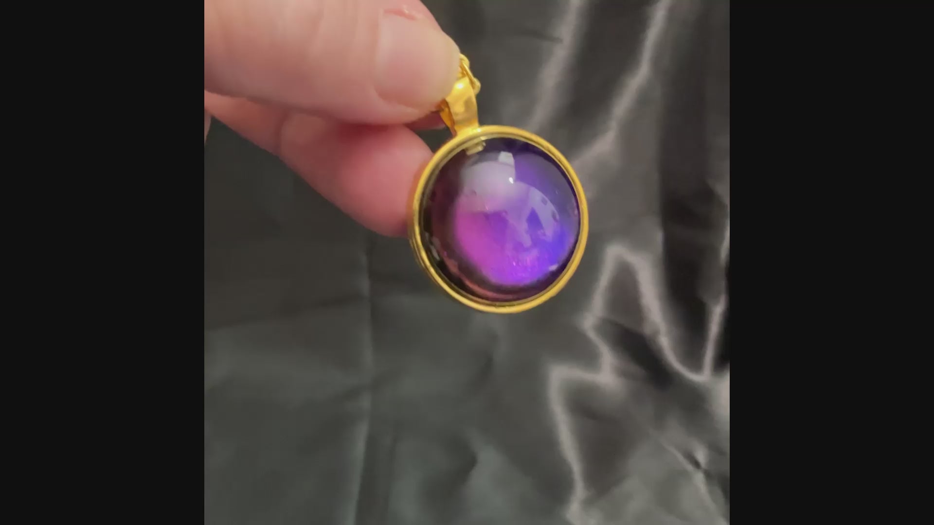 Video showing how the gold plated handmade round resin color shift pendant shifts from blue to purple and other colors depending on how the light hits it.