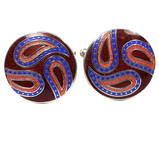 Front view of the retro vintage Joseph Abboud cufflinks. They are round with silver tone color metal. There is a paisley design with blue and red curved teardrops and a darker red enameled background.