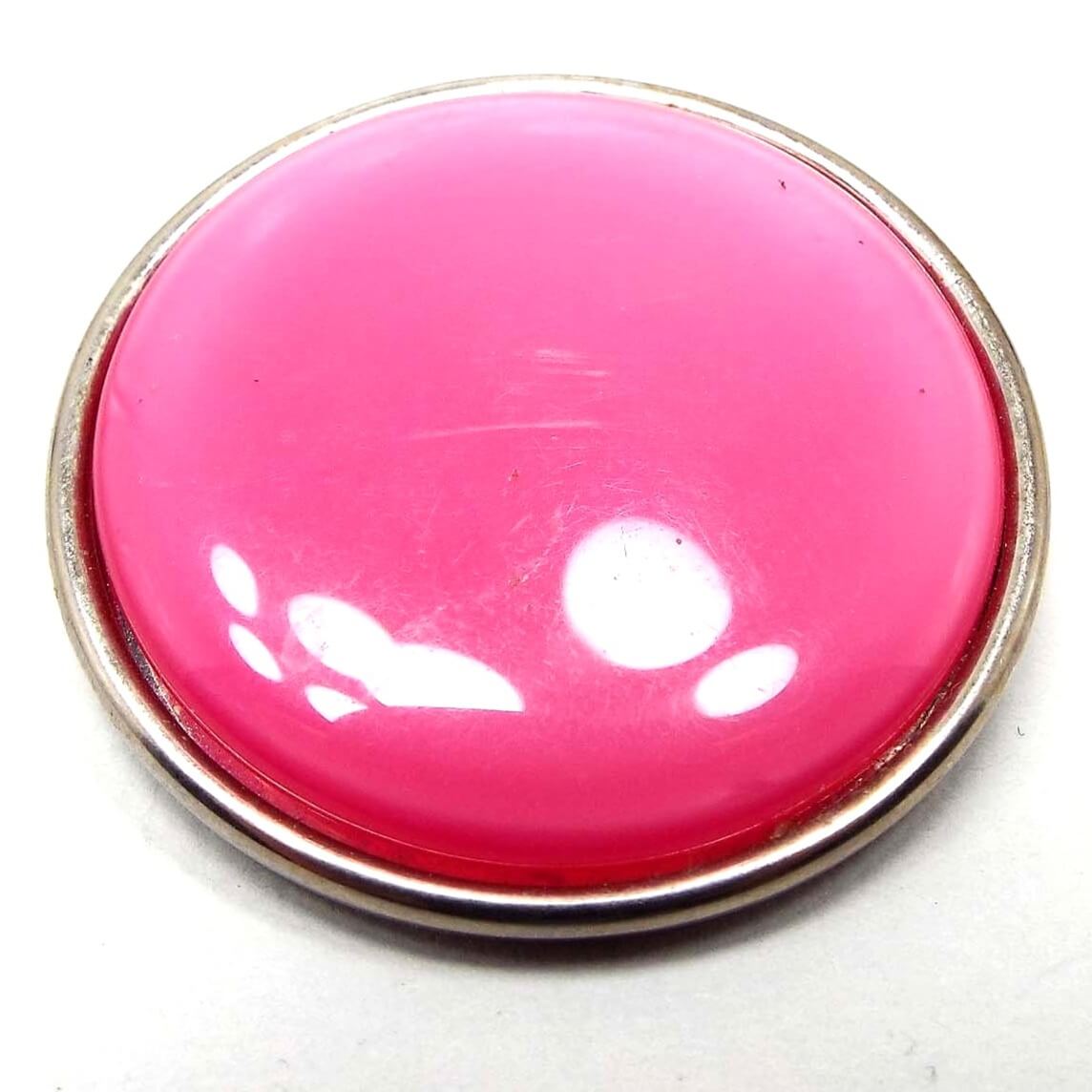 Front view of the Mid Century vintage moonglow lucite scarf clip. It is round and pink in color. The setting is silver tone color metal. Some scuff scratching from age can be seen on the plastic cab. Whites spots showing are reflections from lights during photography.