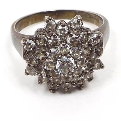 Front view of the retro vintage sterling silver cubic zirconia cocktail ring. The tope has a large flower like cluster of small round prong set CZ stones. There is a larger one in the very middle. The sterling is slightly darkened from age.