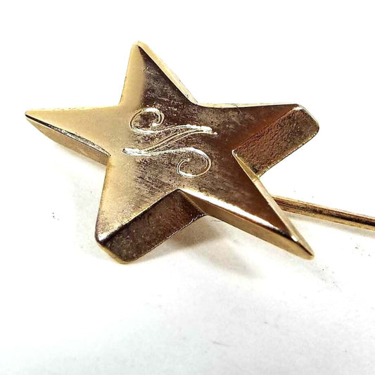 Enlarged view of the top of the Mid Century vintage initial stick pin. The metal is gold tone in color. There is a star shape at the top with a fancy script letter N engraved on it.
