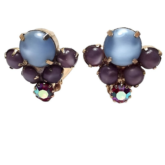 Front view of the Mid Century vintage clip on earrings. The metal is gold tone in color. There is a large round blue moonglow cab at the top with two round purple moonglow cabs at each side on the bottom at an angle for a V like shape. At the very bottom is a round AB red rhinestone.