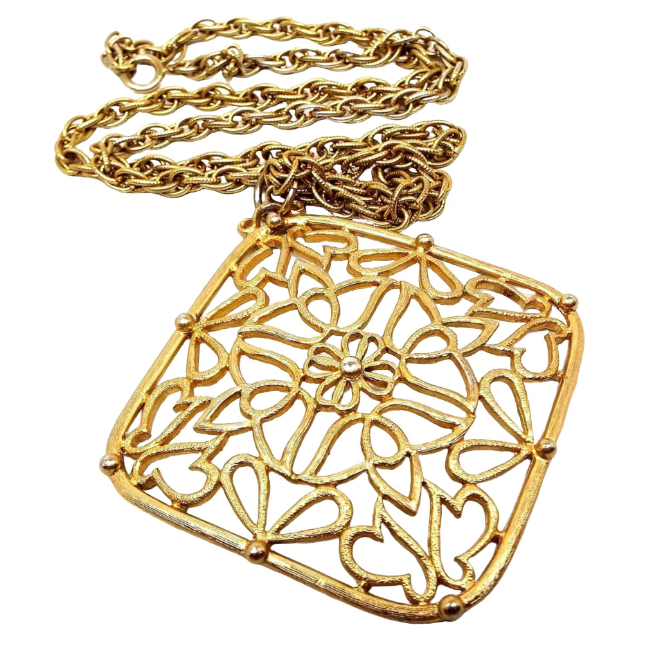 Front view of the retro vintage JJ pendant necklace. The metal is gold tone in color. There is a twisted rope chain with a spring ring clasp. The large pendant is square shaped hanging from one of the corners and h as a filigree design with a small flower in the middle.
