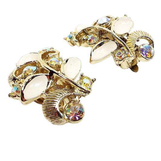 Clip on earrings are gold in color. They have a curved design with leaves curved off the stem. Some of the leaves are textured gold color metal and some are curved oval shape with cream color enamel paint on them. Each earring has 6 AB rhinestones in between the leaves that have flashes of different colors as you move around.