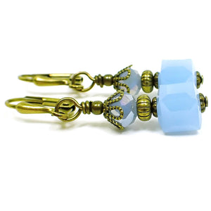 Side view of the small glass beaded earrings. The metal is antiqued brass in color. There are faceted glass crystal rondelle beads at the top and small cube shaped glass beads at the bottom. The beads are light blue in color.